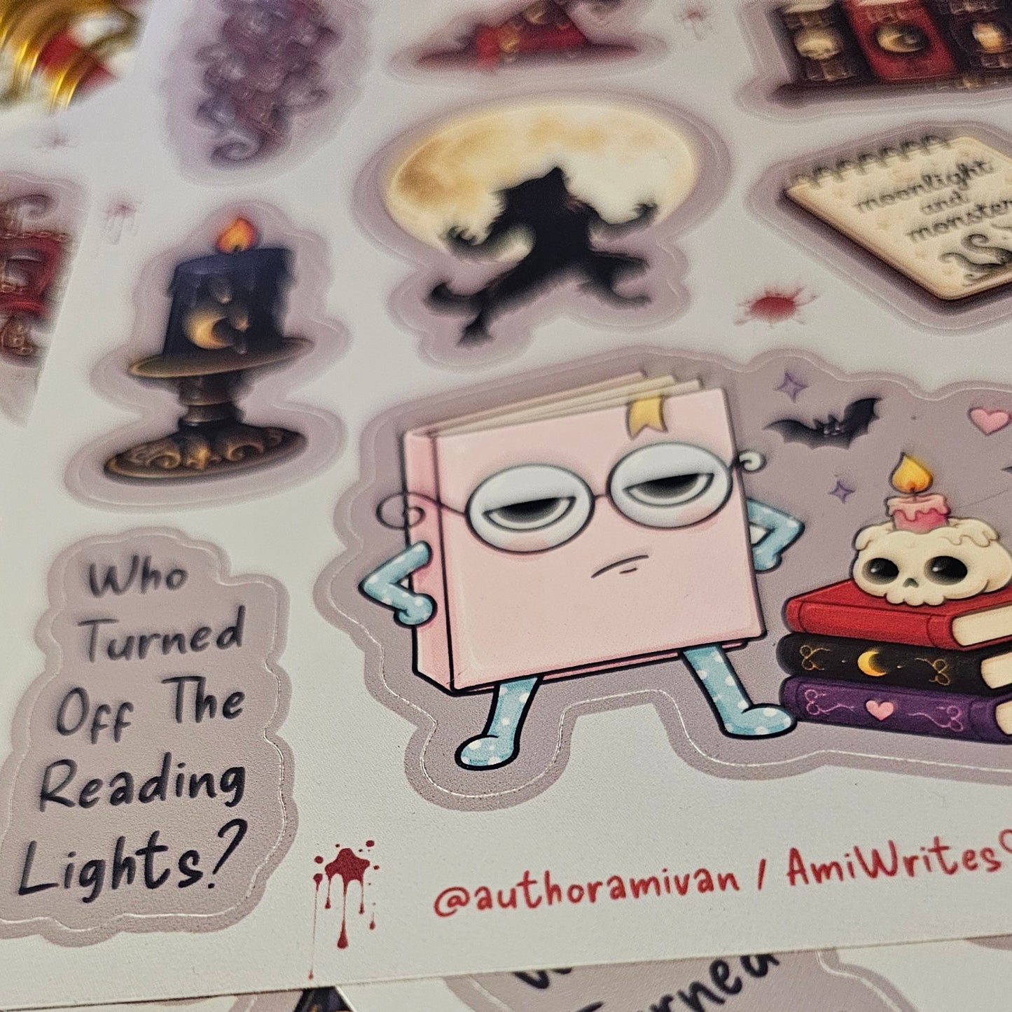 A close-up of printed sticker sheets featuring whimsical book-themed illustrations and text, including a cartoon book character with glasses and the phrase 'Who Turned Off The Reading Lights?'.
