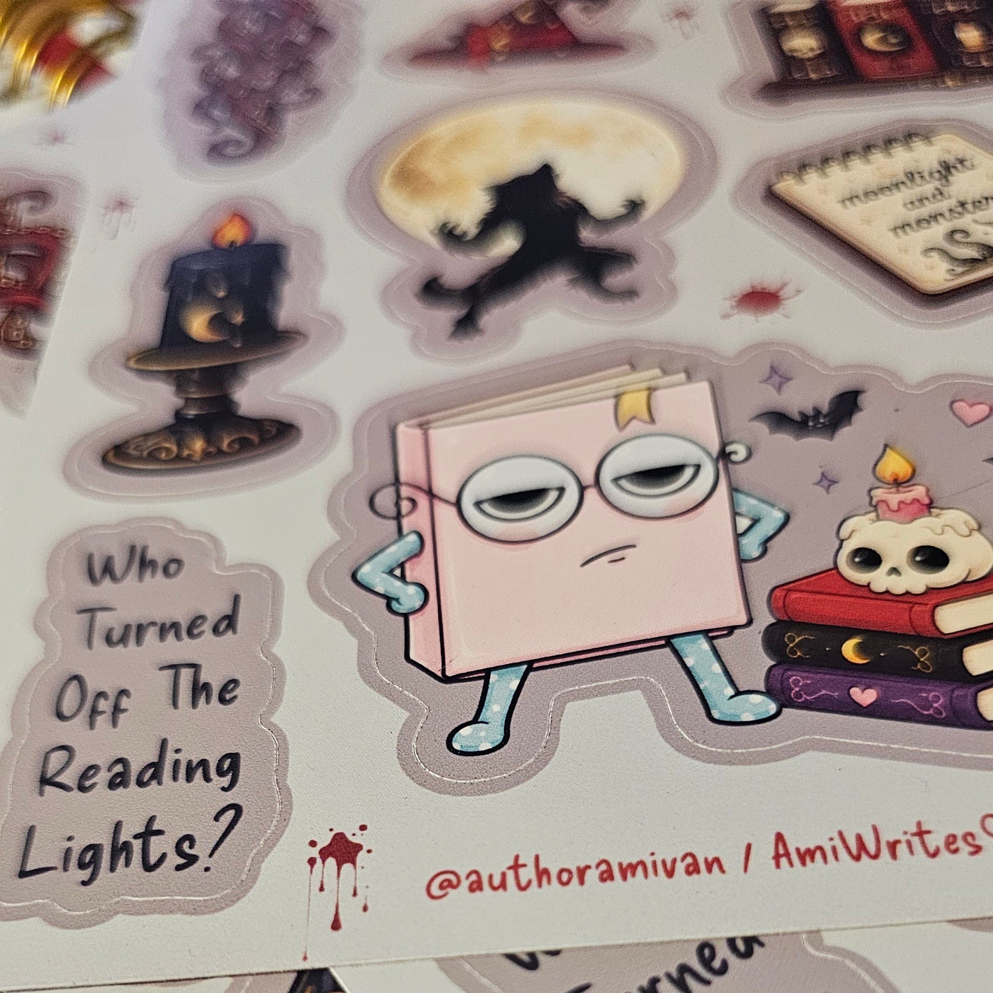 A close-up of printed sticker sheets featuring whimsical book-themed illustrations and text, including a cartoon book character with glasses and the phrase 'Who Turned Off The Reading Lights?'.