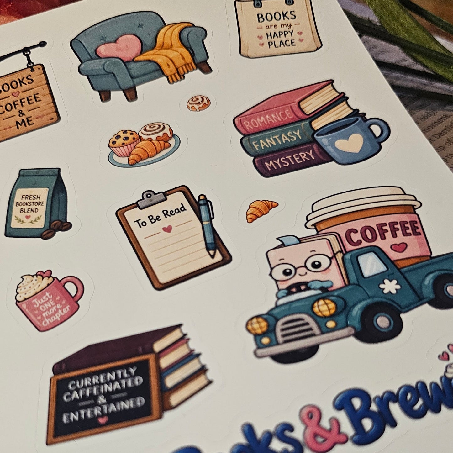 A sheet of cute, colorful book-themed stickers displayed on a white surface. The stickers feature illustrations of cozy reading accessories like a blue armchair with a yellow blanket, a shopping bag reading 'BOOKS HAPPY PLACE', a coffee cup, a vintage truck carrying a coffee canister, and a clipboard that says 'TO BE READ'.