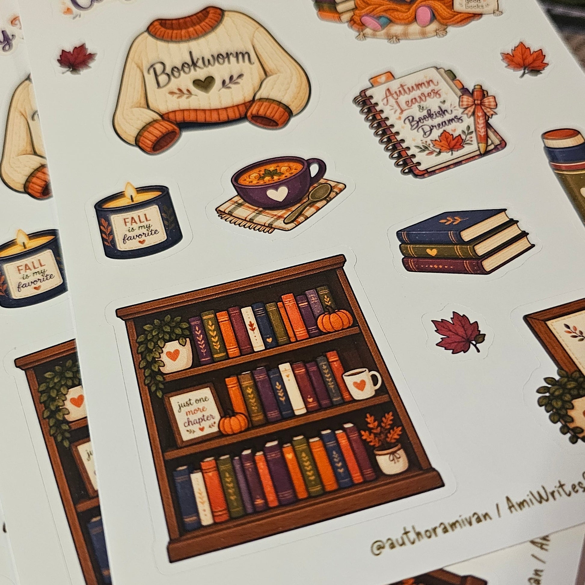 A stack of printed sticker sheets featuring cozy fall-themed illustrations, including a sweater that says 'Bookworm', books, a bookshelf, autumn leaves, and handwritten-style titles like 'Cozy Fall Reads'.