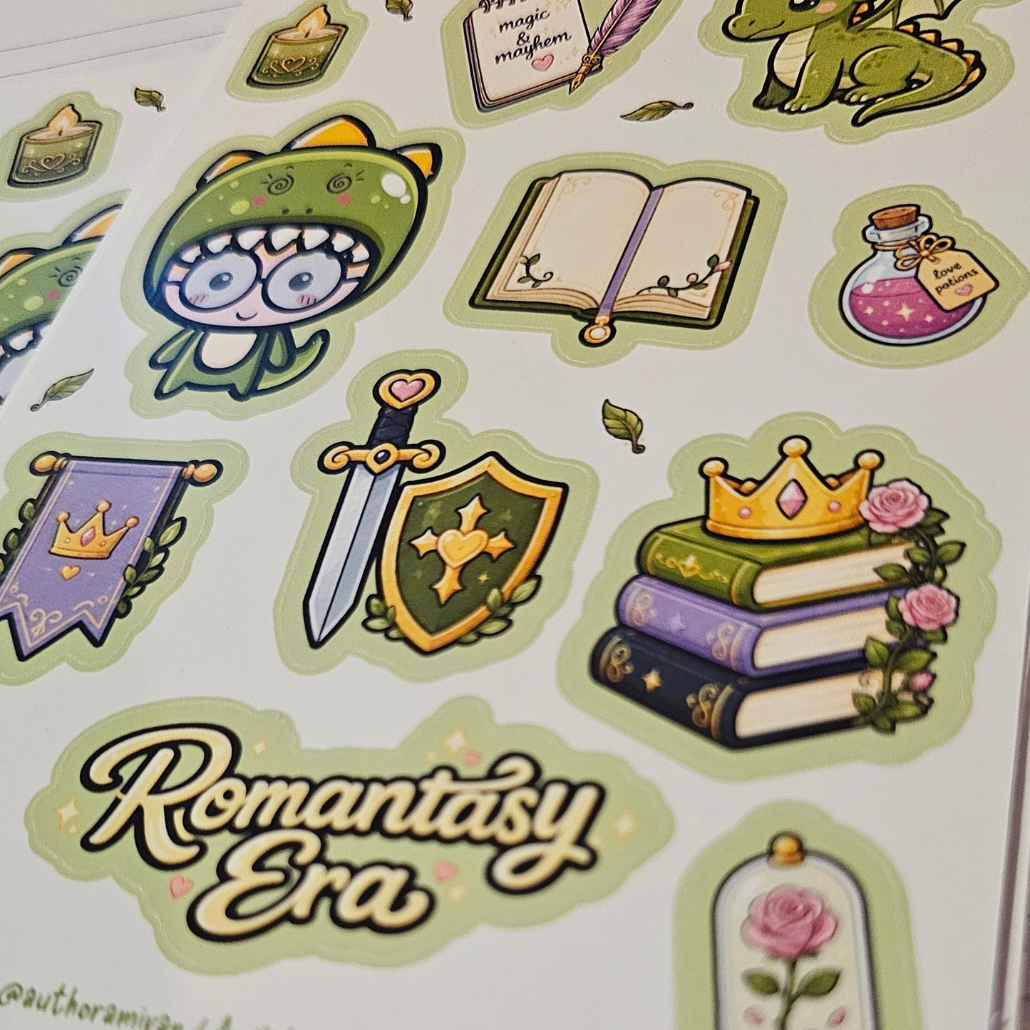 A sheet of cute fantasy-themed stickers displayed on a planner page. The stickers feature illustrations of a green dragon, an owl in a knight helmet, books, a sword, a crown, a cloche with a rose, and banners.