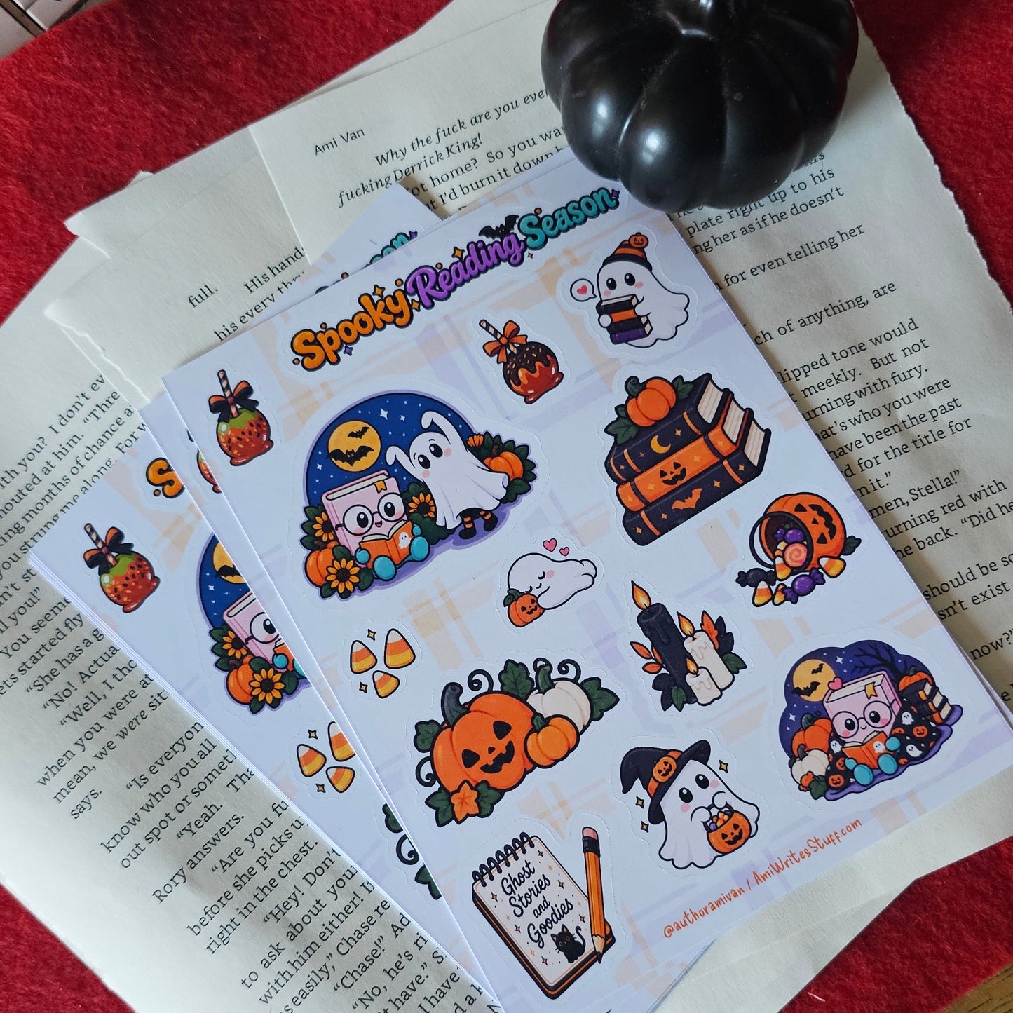 A sheet of Halloween-themed stickers or decals laid on top of printed papers, with a small black pumpkin-shaped object nearby. The sticker sheet features cartoon ghosts, pumpkins, a witch, candy corn, and other spooky illustrations on a white background.