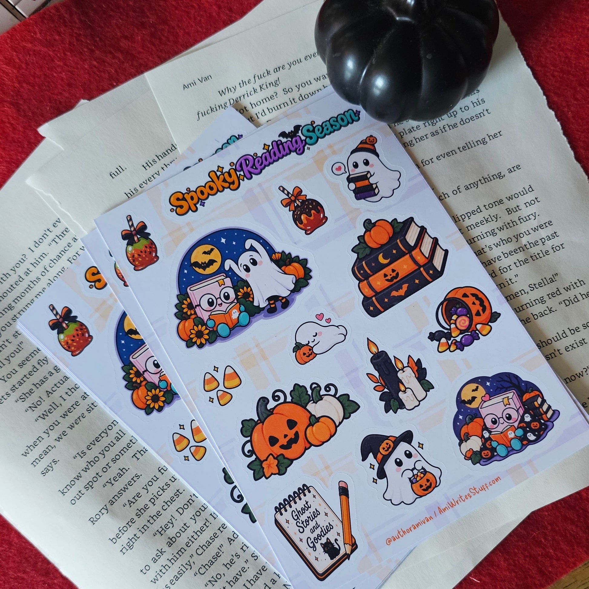 A sheet of Halloween-themed stickers or decals laid on top of printed papers, with a small black pumpkin-shaped object nearby. The sticker sheet features cartoon ghosts, pumpkins, a witch, candy corn, and other spooky illustrations on a white background.